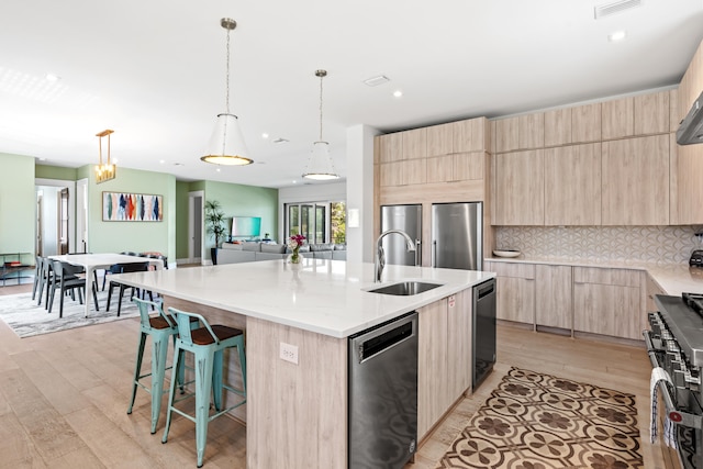 kitchen with tasteful backsplash, an island with sink, light wood-type flooring, appliances with stainless steel finishes, and sink