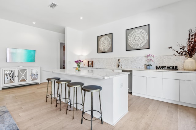 kitchen with light hardwood / wood-style flooring, backsplash, a center island, white cabinets, and a kitchen bar