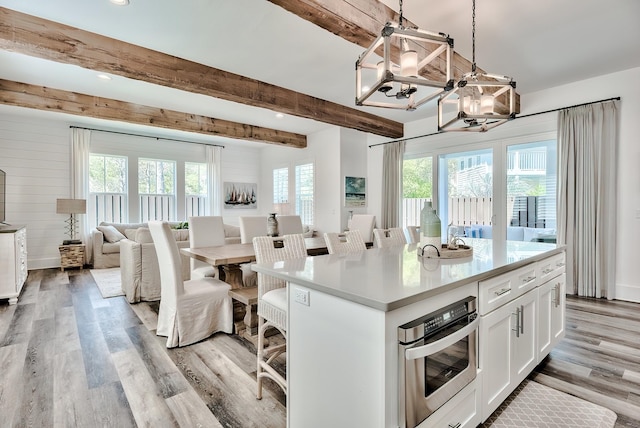 kitchen featuring white cabinetry, a kitchen island, light wood-type flooring, beamed ceiling, and stainless steel oven