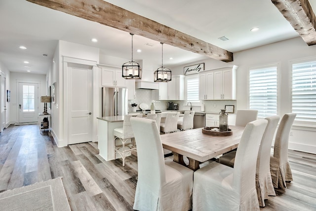 dining area featuring beam ceiling, a healthy amount of sunlight, sink, and light wood-type flooring