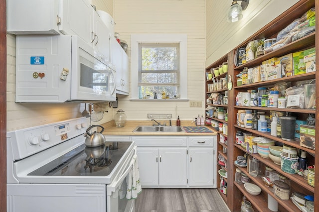 kitchen with wooden walls, stove, white cabinets, and sink