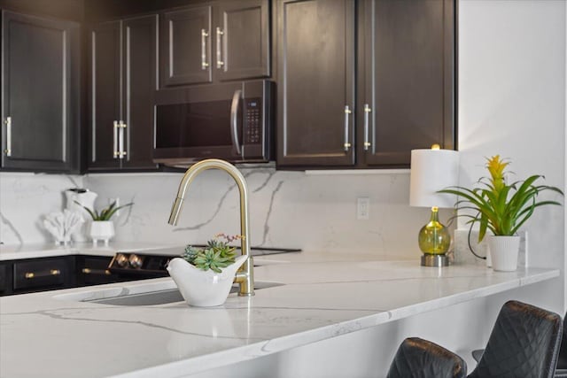 kitchen with light stone countertops, dark brown cabinets, and backsplash