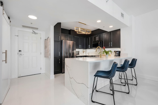 kitchen with a kitchen breakfast bar, kitchen peninsula, a barn door, stainless steel refrigerator, and tasteful backsplash