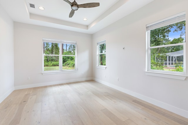 unfurnished room featuring a raised ceiling, ceiling fan, and light wood-type flooring