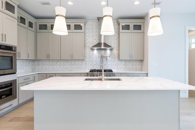 kitchen with stainless steel oven, a kitchen island with sink, and hanging light fixtures