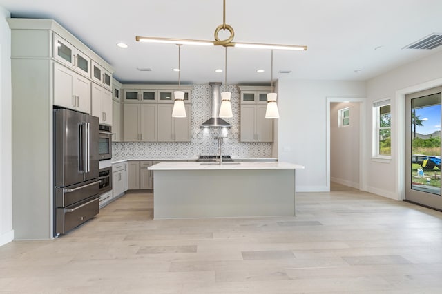 kitchen with an island with sink, backsplash, hanging light fixtures, wall chimney range hood, and high end fridge