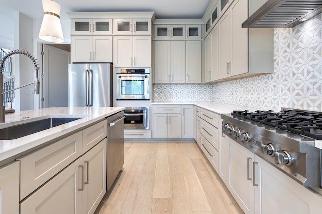 kitchen featuring sink, light hardwood / wood-style floors, tasteful backsplash, custom exhaust hood, and appliances with stainless steel finishes