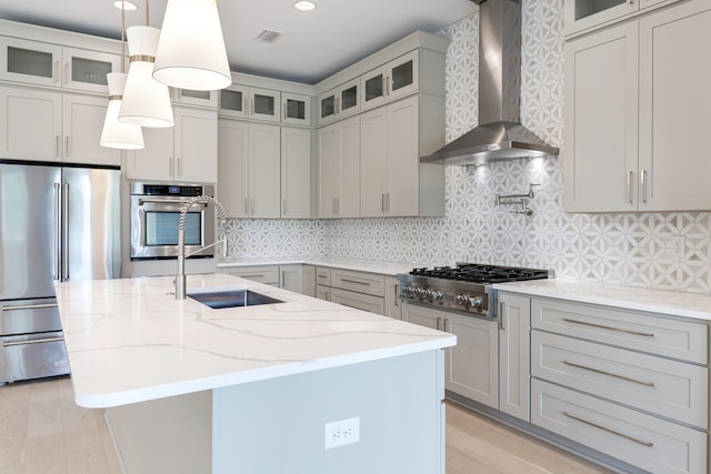 kitchen featuring decorative light fixtures, appliances with stainless steel finishes, wall chimney exhaust hood, and a kitchen island with sink