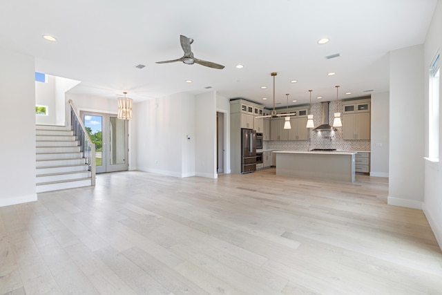 unfurnished living room featuring ceiling fan with notable chandelier and light wood-type flooring