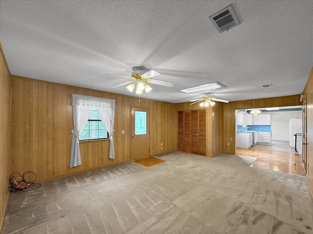 unfurnished living room with light carpet, wooden walls, ceiling fan, and a textured ceiling