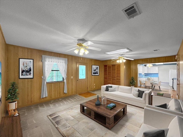 living room with a textured ceiling, a skylight, ceiling fan, and wood walls