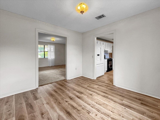 spare room featuring a textured ceiling and light hardwood / wood-style floors