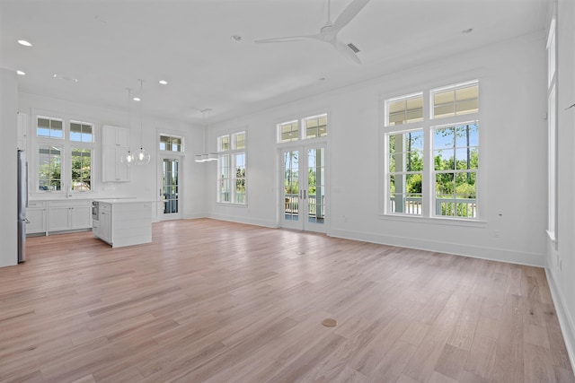 unfurnished living room featuring a wealth of natural light, ceiling fan, and light hardwood / wood-style floors