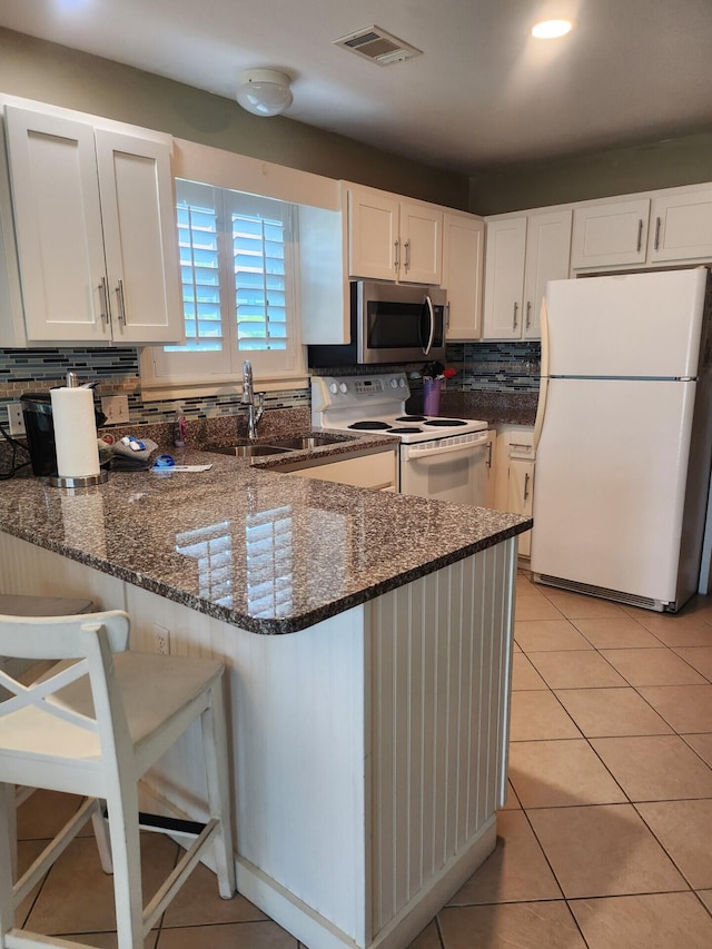 kitchen featuring backsplash, dark stone countertops, and white appliances