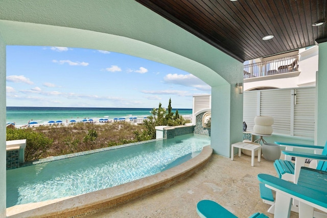 view of patio with a water view, a balcony, and a view of the beach