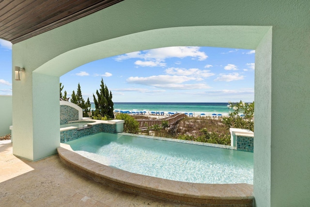 view of pool with a pool with connected hot tub, a water view, and a beach view