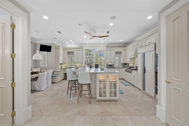 kitchen with a breakfast bar area, a kitchen island with sink, recessed lighting, crown molding, and custom range hood