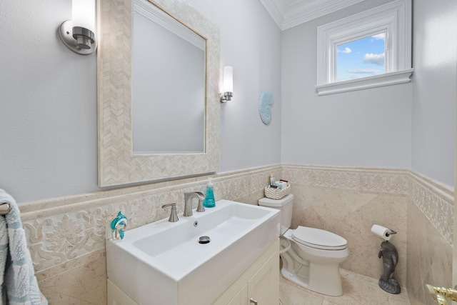 half bathroom with a wainscoted wall, tile walls, toilet, ornamental molding, and vanity