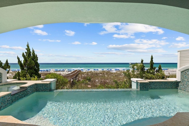 view of pool with a pool with connected hot tub, a water view, and a beach view