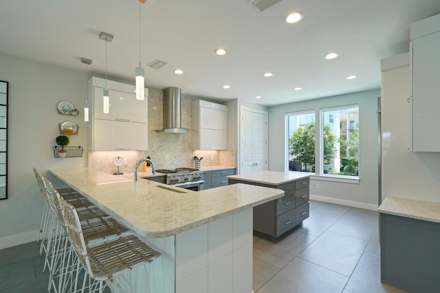 kitchen with tasteful backsplash, decorative light fixtures, a center island, wall chimney exhaust hood, and a kitchen bar