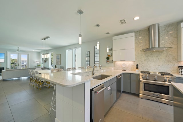 kitchen featuring kitchen peninsula, wall chimney exhaust hood, a breakfast bar area, sink, and appliances with stainless steel finishes