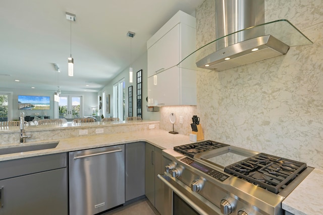 kitchen featuring wall chimney range hood, light stone countertops, stainless steel appliances, and gray cabinetry