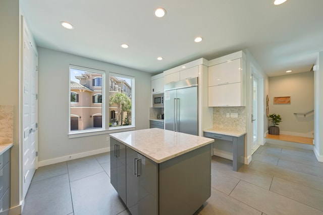 kitchen featuring a center island, white cabinets, built in appliances, backsplash, and light tile floors