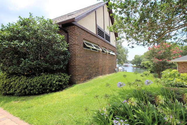 view of side of property featuring a yard, brick siding, a water view, and stucco siding