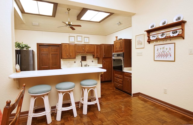 kitchen featuring appliances with stainless steel finishes, brown cabinets, a breakfast bar area, a peninsula, and light countertops