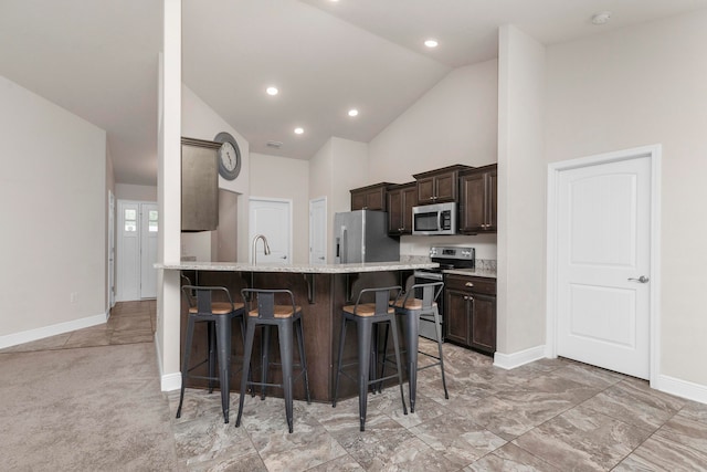 kitchen featuring light stone countertops, high vaulted ceiling, light colored carpet, a breakfast bar, and appliances with stainless steel finishes