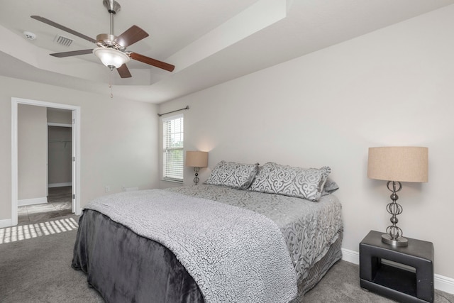 bedroom with carpet flooring, a walk in closet, a tray ceiling, ceiling fan, and a closet