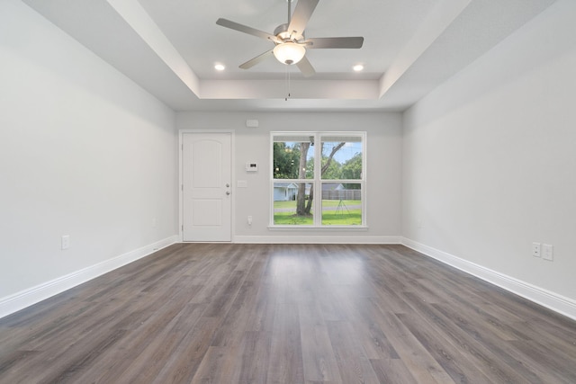 unfurnished room with a raised ceiling, ceiling fan, and dark hardwood / wood-style flooring