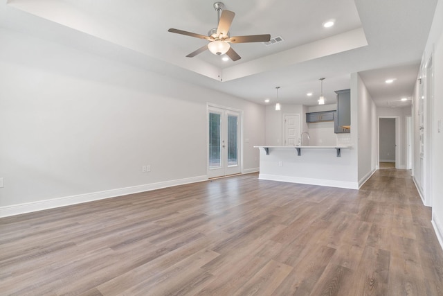 unfurnished living room featuring french doors, ceiling fan, a raised ceiling, and dark hardwood / wood-style floors