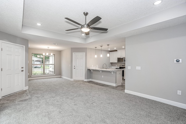 unfurnished living room featuring a textured ceiling, ceiling fan with notable chandelier, carpet, and a raised ceiling