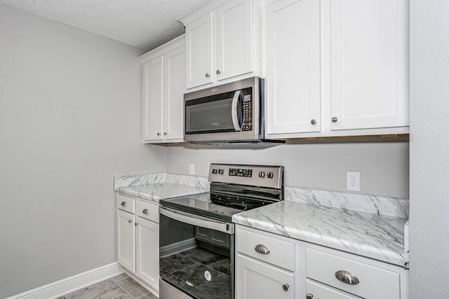 kitchen with white cabinetry, light stone counters, appliances with stainless steel finishes, and a textured ceiling