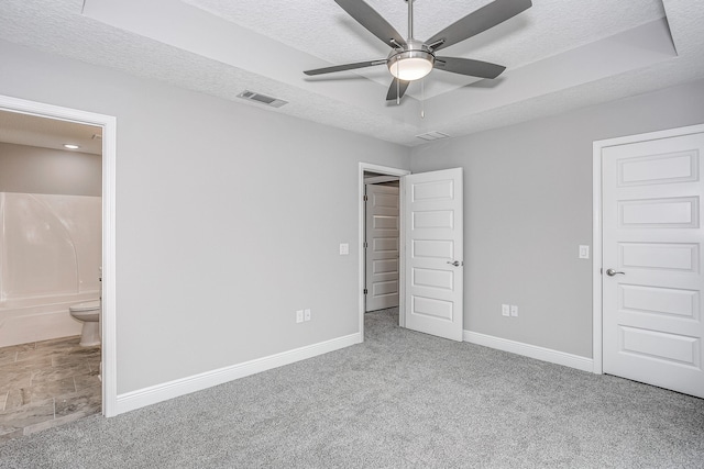 unfurnished bedroom featuring a textured ceiling, ensuite bathroom, light colored carpet, and ceiling fan