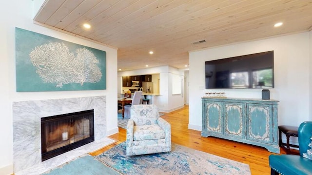 living room featuring a premium fireplace, light wood-type flooring, and wood ceiling