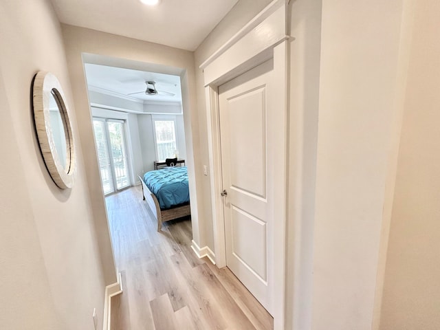 corridor with light hardwood / wood-style floors and crown molding