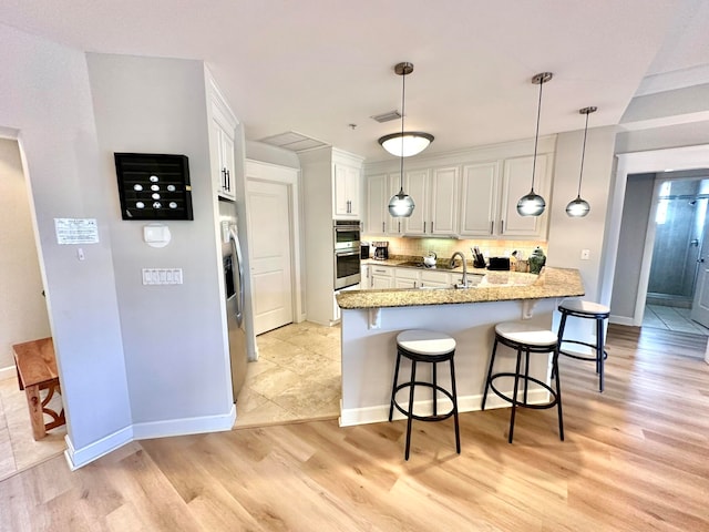 kitchen featuring light wood-type flooring, appliances with stainless steel finishes, hanging light fixtures, white cabinets, and kitchen peninsula