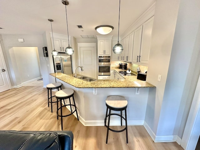 kitchen featuring stainless steel appliances, hanging light fixtures, sink, a breakfast bar area, and light wood-type flooring