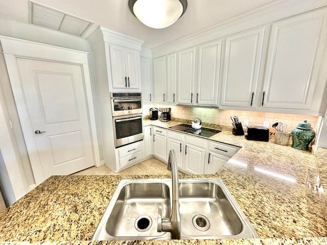 kitchen featuring light stone countertops, stainless steel double oven, white cabinetry, and sink