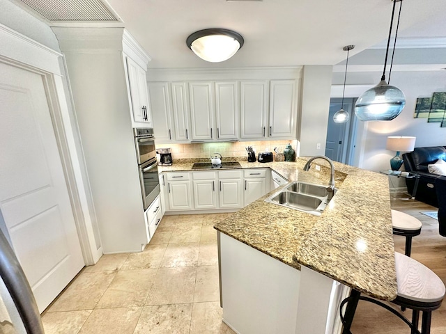 kitchen featuring pendant lighting, sink, a breakfast bar area, black stovetop, and white cabinetry