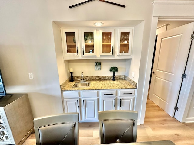 bar featuring white cabinetry, light hardwood / wood-style flooring, sink, and light stone countertops