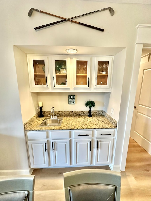 bar with white cabinets, light wood-type flooring, sink, and light stone counters