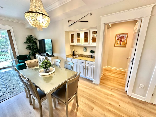 dining space with light hardwood / wood-style floors, a notable chandelier, sink, and crown molding