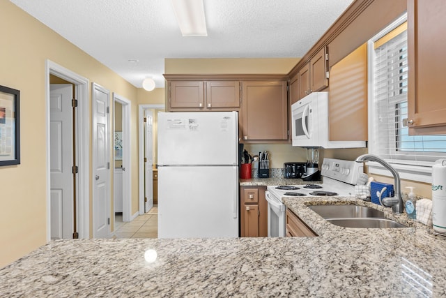 kitchen with a textured ceiling, white appliances, light stone counters, sink, and light tile floors