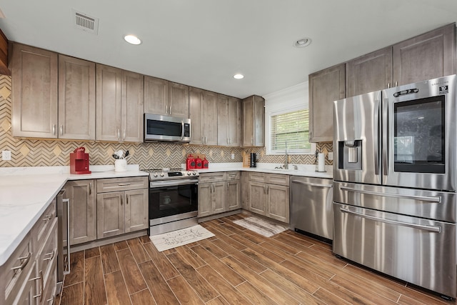 kitchen featuring backsplash, light stone counters, stainless steel appliances, dark wood-type flooring, and sink