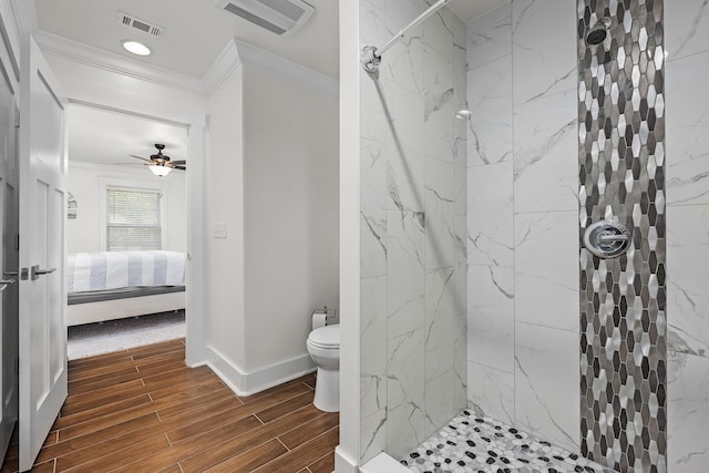 bathroom with a tile shower, toilet, ceiling fan, and crown molding