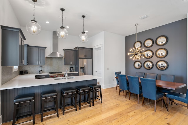 kitchen featuring light hardwood / wood-style floors, stainless steel fridge, wall chimney exhaust hood, sink, and tasteful backsplash