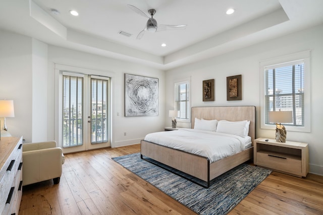 bedroom featuring ceiling fan, light hardwood / wood-style floors, a tray ceiling, french doors, and access to outside